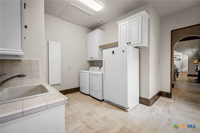 washroom featuring arched walkways, washing machine and clothes dryer, cabinet space, attic access, and a sink