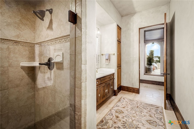 full bath featuring tiled shower, vanity, and baseboards