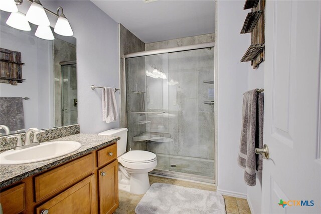 bathroom with a shower with shower door, vanity, toilet, and tile patterned flooring