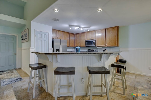 126 Breezy St, Rockport, TX 78382 - kitchen featuring stainless steel appliances, a wainscoted wall, a kitchen bar, brown cabinets, and dark stone countertops