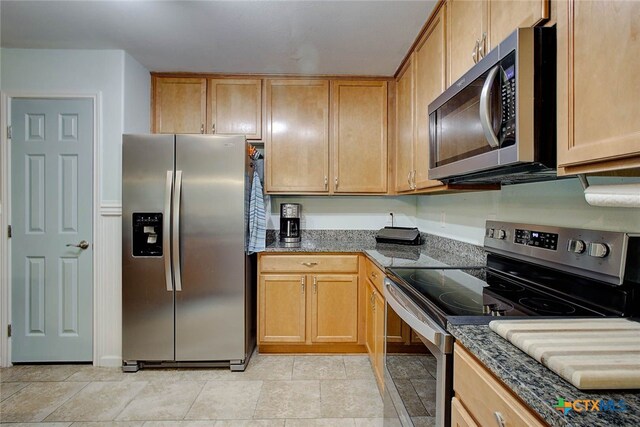 kitchen with stainless steel appliances, dark stone counters, and light tile patterned floors