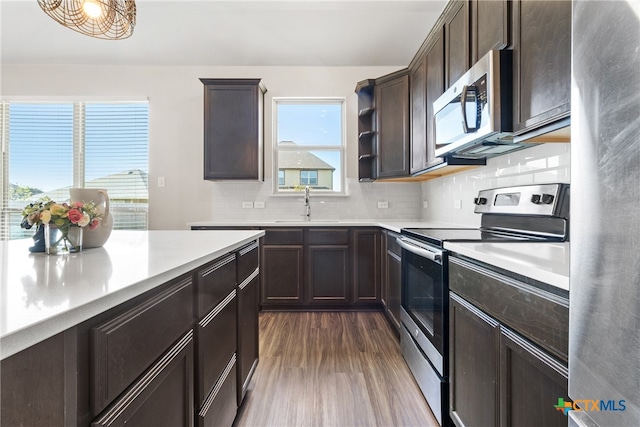 kitchen with dark brown cabinetry, sink, dark wood-type flooring, stainless steel appliances, and tasteful backsplash