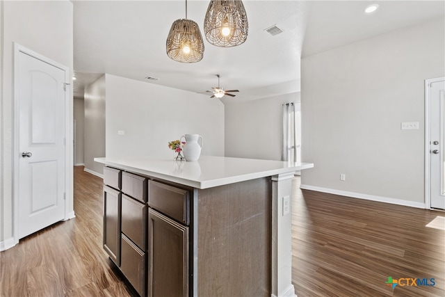 kitchen featuring decorative light fixtures, a kitchen island, dark brown cabinetry, and dark wood-type flooring