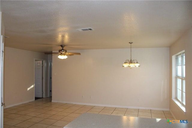 spare room featuring ceiling fan with notable chandelier, light tile patterned floors, and a textured ceiling