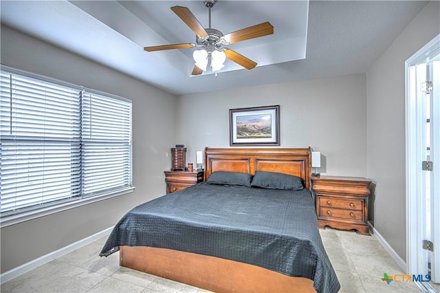 bedroom featuring tile patterned flooring, a raised ceiling, a ceiling fan, and baseboards