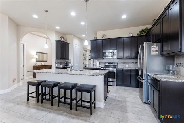 702 Old Settlers Dr, San Marcos, TX 78666 - kitchen featuring stainless steel appliances, a breakfast bar, a sink, arched walkways, and light stone counters