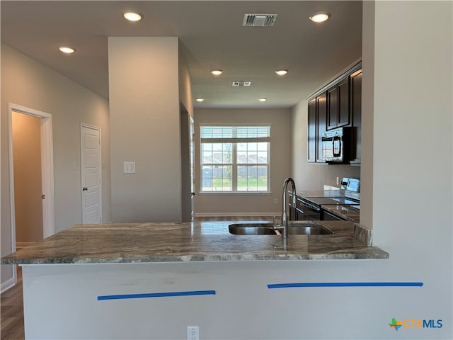 kitchen with light stone counters, dark hardwood / wood-style floors, sink, kitchen peninsula, and stainless steel electric stove