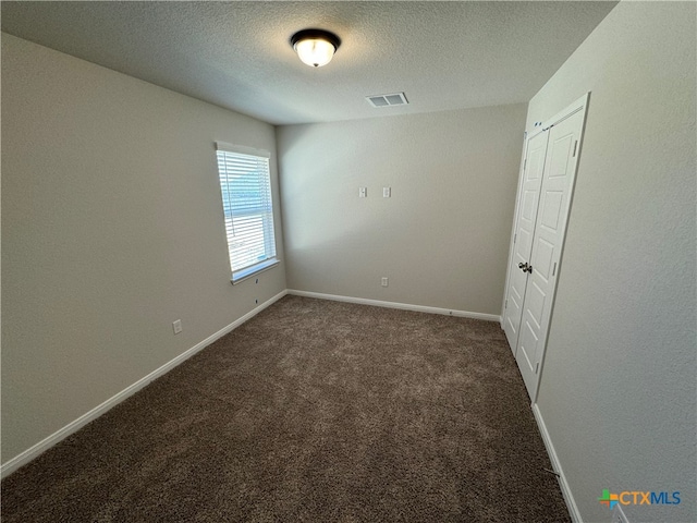 unfurnished bedroom with dark colored carpet, a textured ceiling, and a closet