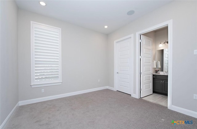 unfurnished bedroom featuring sink, light colored carpet, and ensuite bathroom