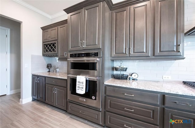 kitchen featuring dark brown cabinetry, crown molding, double oven, light stone countertops, and decorative backsplash