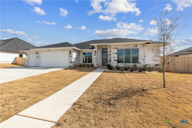 view of front of property featuring stone siding, fence, driveway, and an attached garage