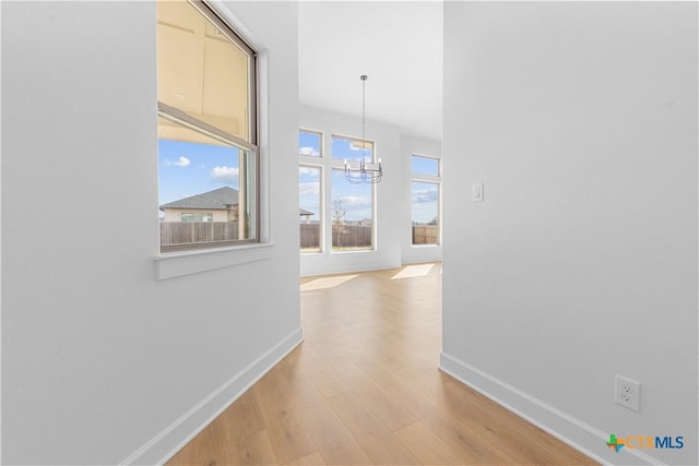 hallway featuring a chandelier, light wood-style flooring, and baseboards