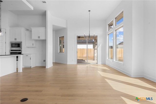 interior space with visible vents, light wood-style flooring, baseboards, and an inviting chandelier