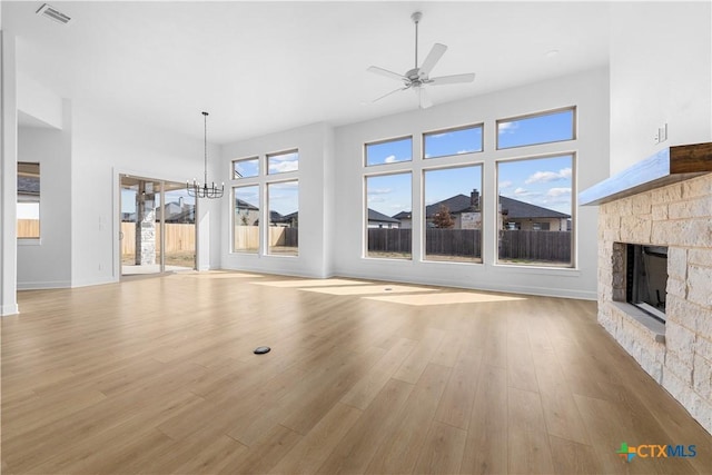 unfurnished living room featuring baseboards, visible vents, wood finished floors, a fireplace, and ceiling fan with notable chandelier