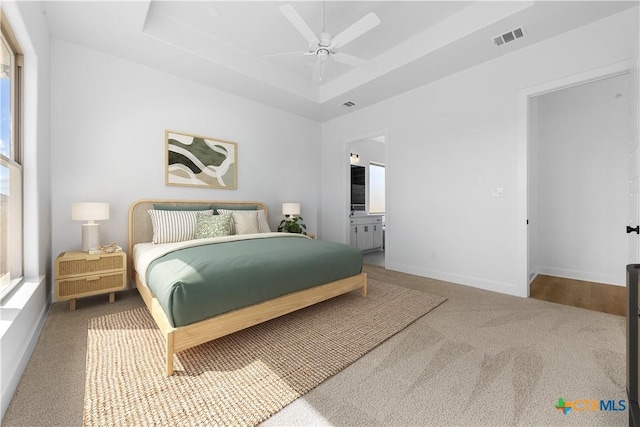 carpeted bedroom with connected bathroom, a raised ceiling, visible vents, and baseboards