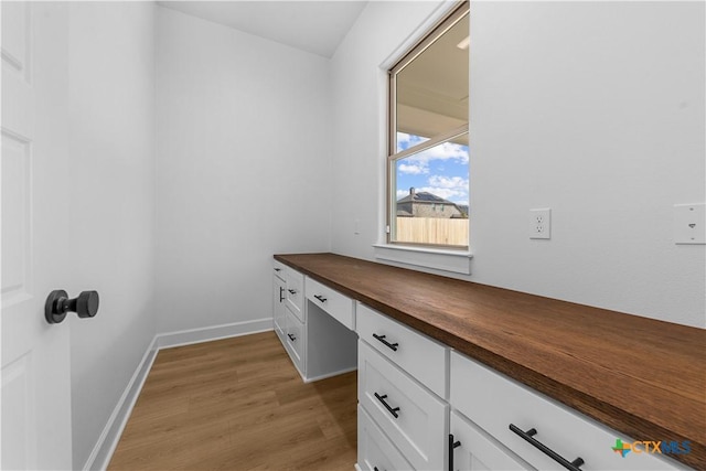 unfurnished office featuring built in desk, light wood-type flooring, and baseboards