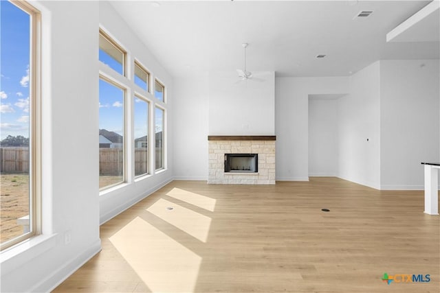 unfurnished living room featuring visible vents, light wood-style flooring, ceiling fan, a stone fireplace, and baseboards