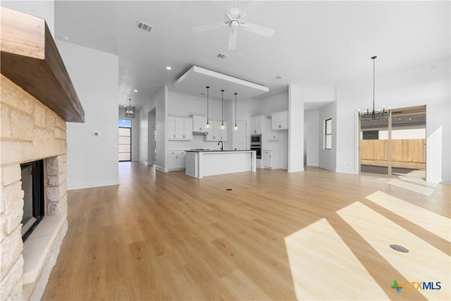 unfurnished living room with a fireplace, visible vents, light wood-style flooring, a sink, and ceiling fan with notable chandelier