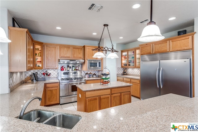 kitchen with light stone counters, built in appliances, sink, backsplash, and pendant lighting