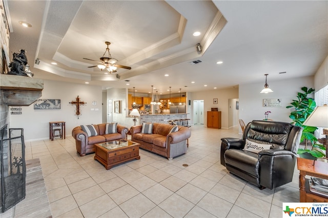 living room featuring a tray ceiling, light tile patterned floors, ceiling fan, and crown molding