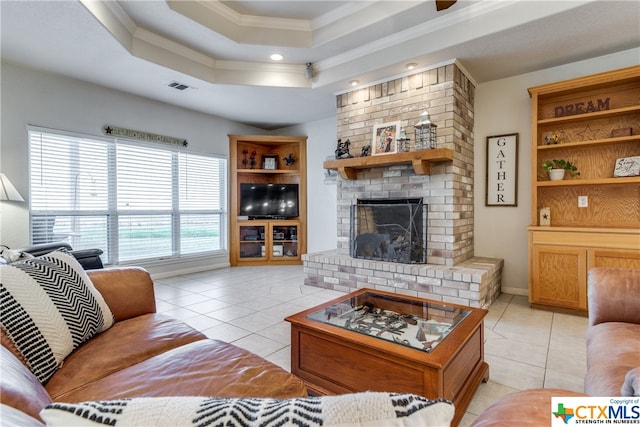 living room with crown molding, a raised ceiling, light tile patterned flooring, and a fireplace