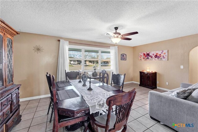 dining area with arched walkways, a textured ceiling, light tile patterned flooring, and ceiling fan
