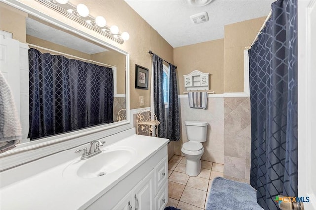 bathroom with tile patterned floors, a textured ceiling, toilet, vanity, and tile walls