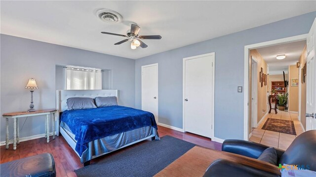 bedroom featuring visible vents, baseboards, ceiling fan, multiple closets, and wood finished floors