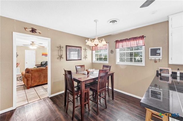 dining room with ceiling fan with notable chandelier and dark hardwood / wood-style flooring