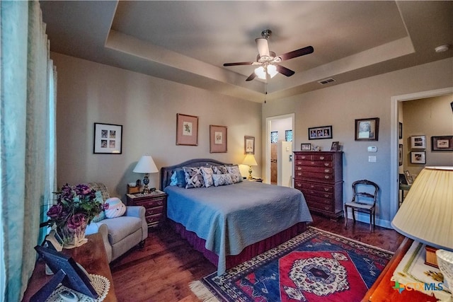 bedroom featuring a ceiling fan, a tray ceiling, visible vents, and wood finished floors