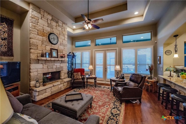 living area with a fireplace, wood finished floors, a ceiling fan, french doors, and a raised ceiling