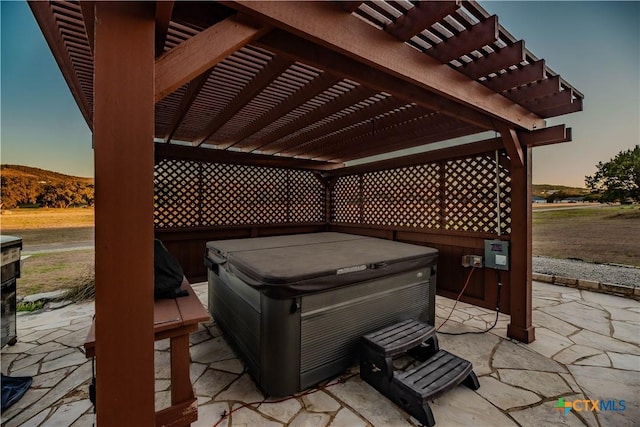 patio terrace at dusk featuring a mountain view, a hot tub, and a pergola