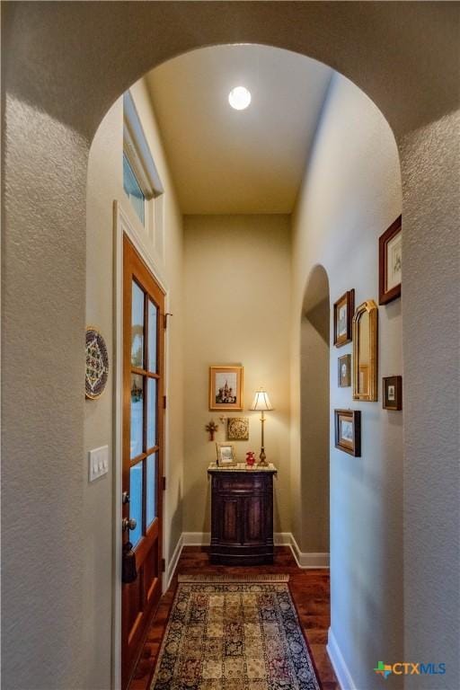 corridor featuring baseboards, arched walkways, and dark wood-type flooring