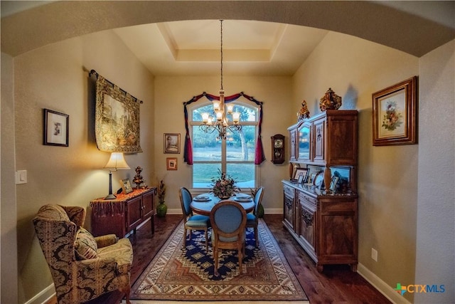 dining room featuring arched walkways, dark wood-type flooring, baseboards, a raised ceiling, and an inviting chandelier