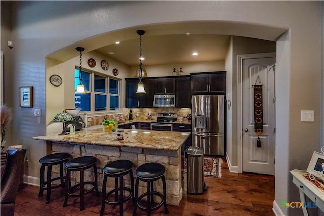 kitchen with appliances with stainless steel finishes, dark wood finished floors, a breakfast bar area, and light stone countertops