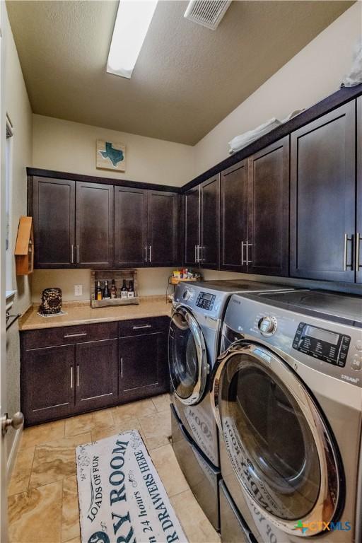 laundry area with visible vents, a textured ceiling, washing machine and dryer, and cabinet space