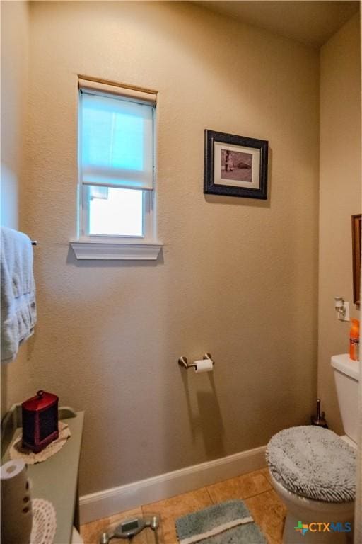 half bath featuring baseboards, toilet, and tile patterned floors