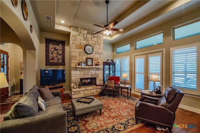 living area with arched walkways, a fireplace, wood finished floors, baseboards, and a tray ceiling