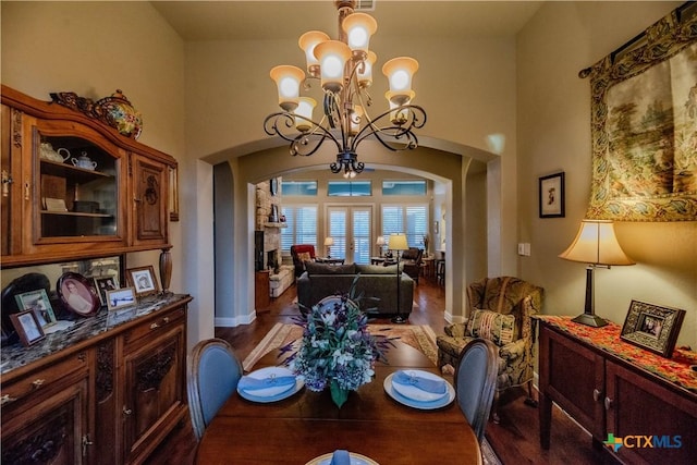 dining room with arched walkways, dark wood-type flooring, an inviting chandelier, a high ceiling, and a fireplace