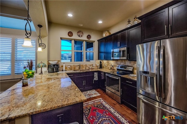 kitchen featuring light stone counters, stainless steel appliances, tasteful backsplash, a sink, and a peninsula