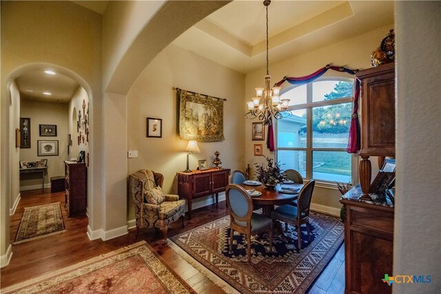 dining area featuring arched walkways, a raised ceiling, wood finished floors, a chandelier, and baseboards