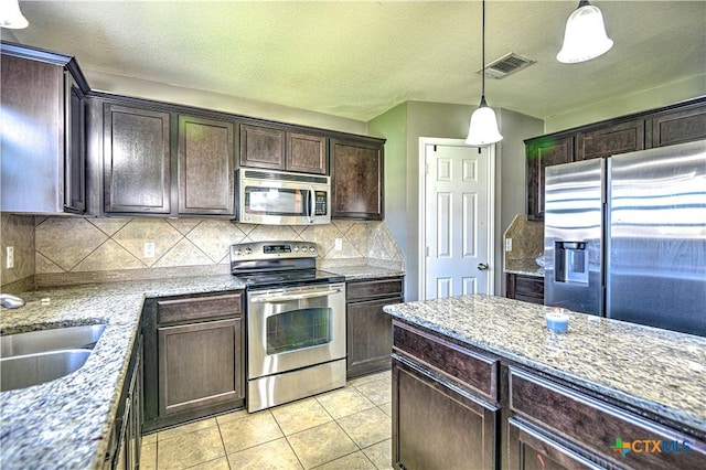 9505 Shimla Dr, Killeen, TX 76542 - kitchen featuring appliances with stainless steel finishes, dark brown cabinetry, decorative backsplash, light tile patterned flooring, and hanging light fixtures