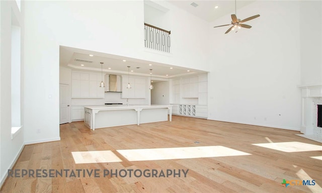 unfurnished living room featuring ceiling fan, light wood-style flooring, a towering ceiling, and a premium fireplace