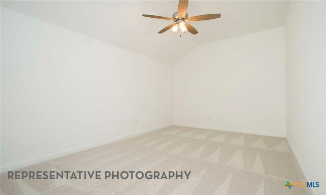 spare room with a ceiling fan, vaulted ceiling, light colored carpet, and baseboards