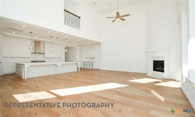 unfurnished living room featuring visible vents, light wood-style flooring, a high ceiling, a premium fireplace, and ceiling fan