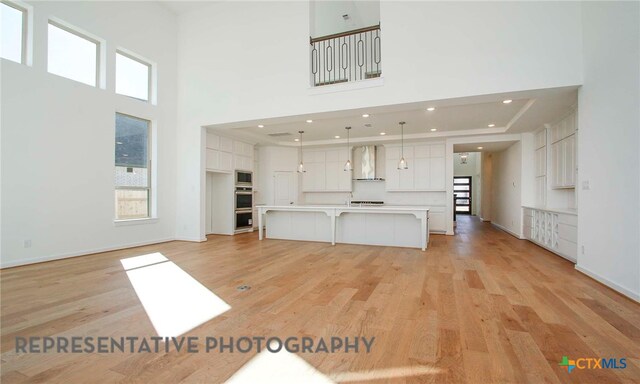 unfurnished living room with a high ceiling, recessed lighting, baseboards, and light wood finished floors