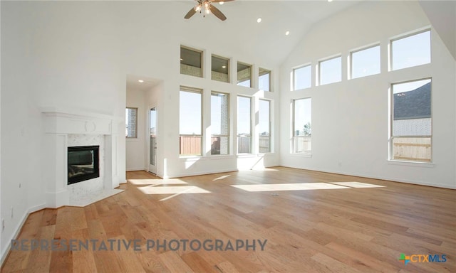 unfurnished living room featuring baseboards, a ceiling fan, a high end fireplace, and light wood finished floors