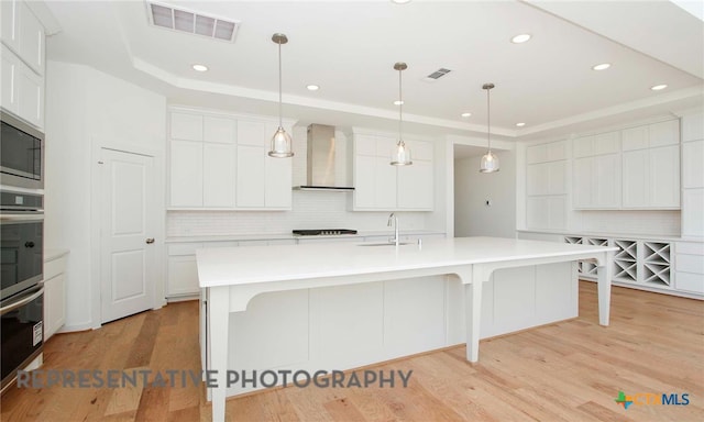 kitchen with visible vents, a raised ceiling, wall chimney exhaust hood, and light wood-style floors