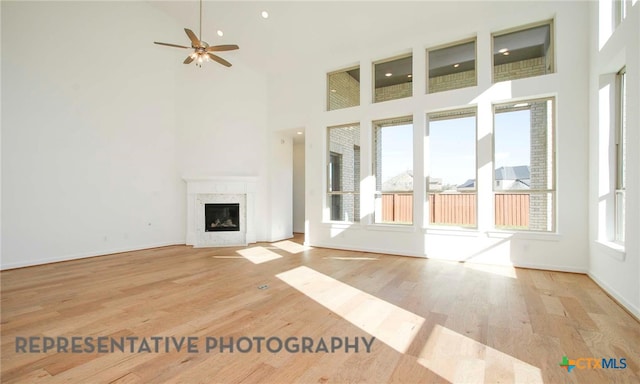 unfurnished living room with wood finished floors, a high ceiling, a ceiling fan, and a premium fireplace