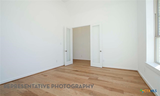 empty room with a towering ceiling, french doors, baseboards, and wood finished floors